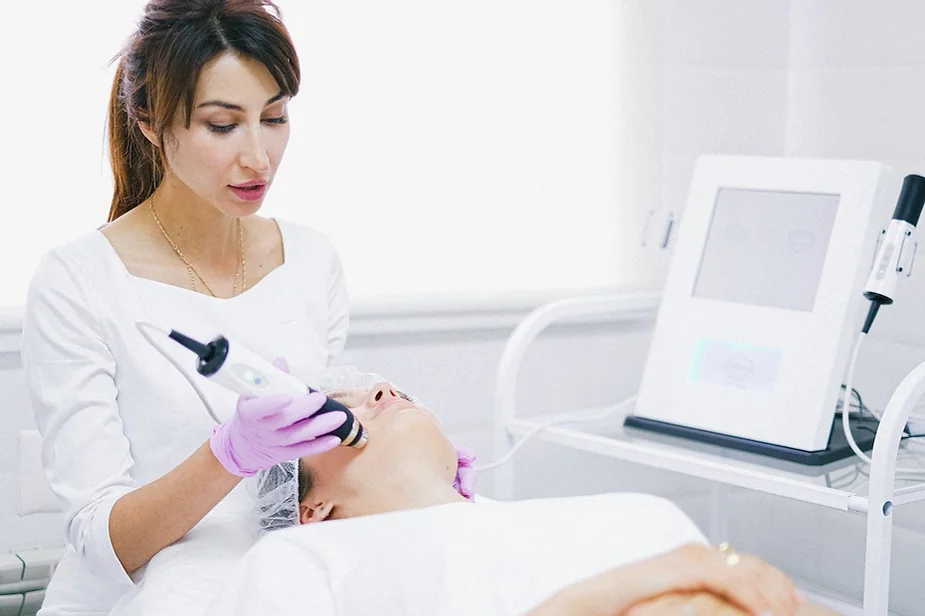 Médica aplicando un tratamiento facial con un equipo de aparatología a una paciente recostada