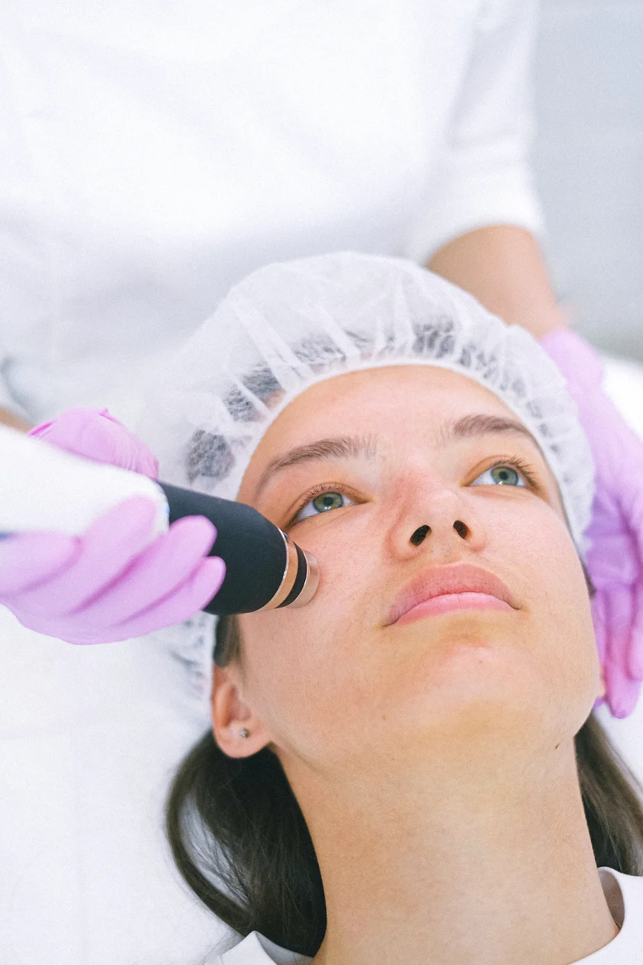 Patient wearing a disposable cap receiving a non-surgical facial treatment with an applicator on her cheek