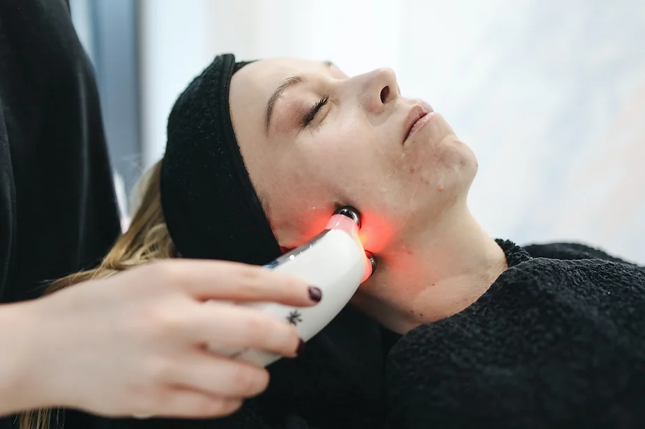 Patient lying down receiving a device-based facial treatment with red light on her jawline