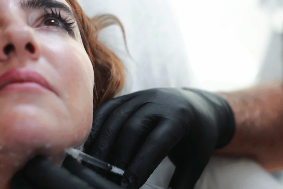 Médico con guantes negros aplicando una inyección en el cuello de una paciente recostada