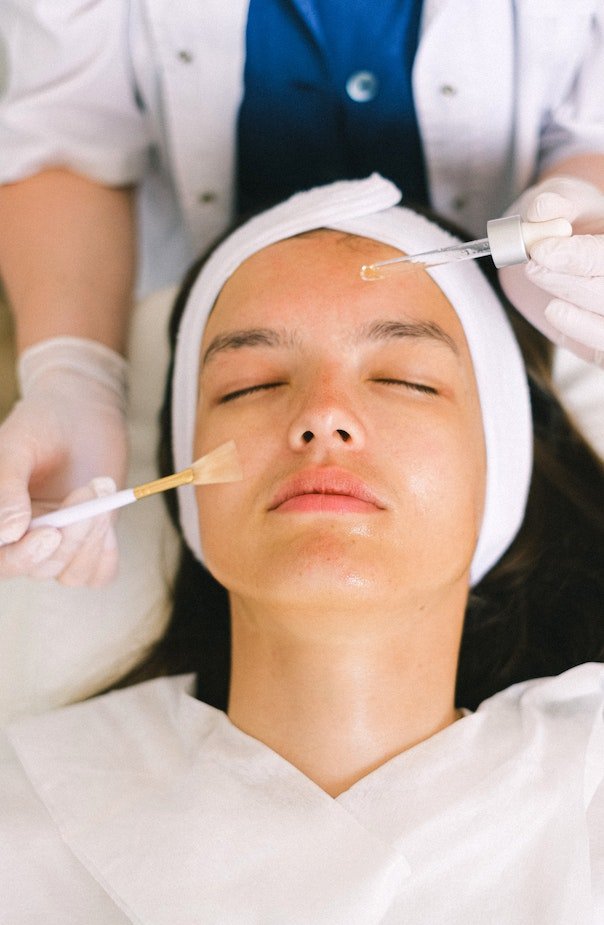Patient lying down with her eyes closed while the physician brushes a peel onto her face