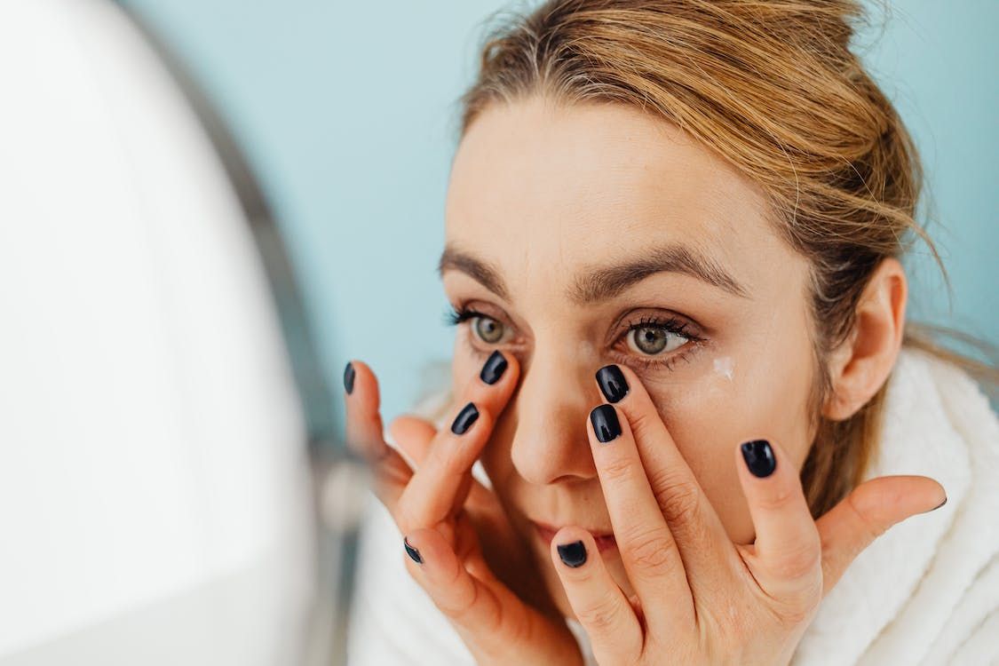 Mujer frente al espejo revisa la piel bajo sus ojos con la punta de los dedos