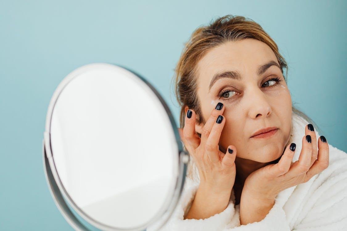 Mature woman looking closely at the skin on her face in a round mirror