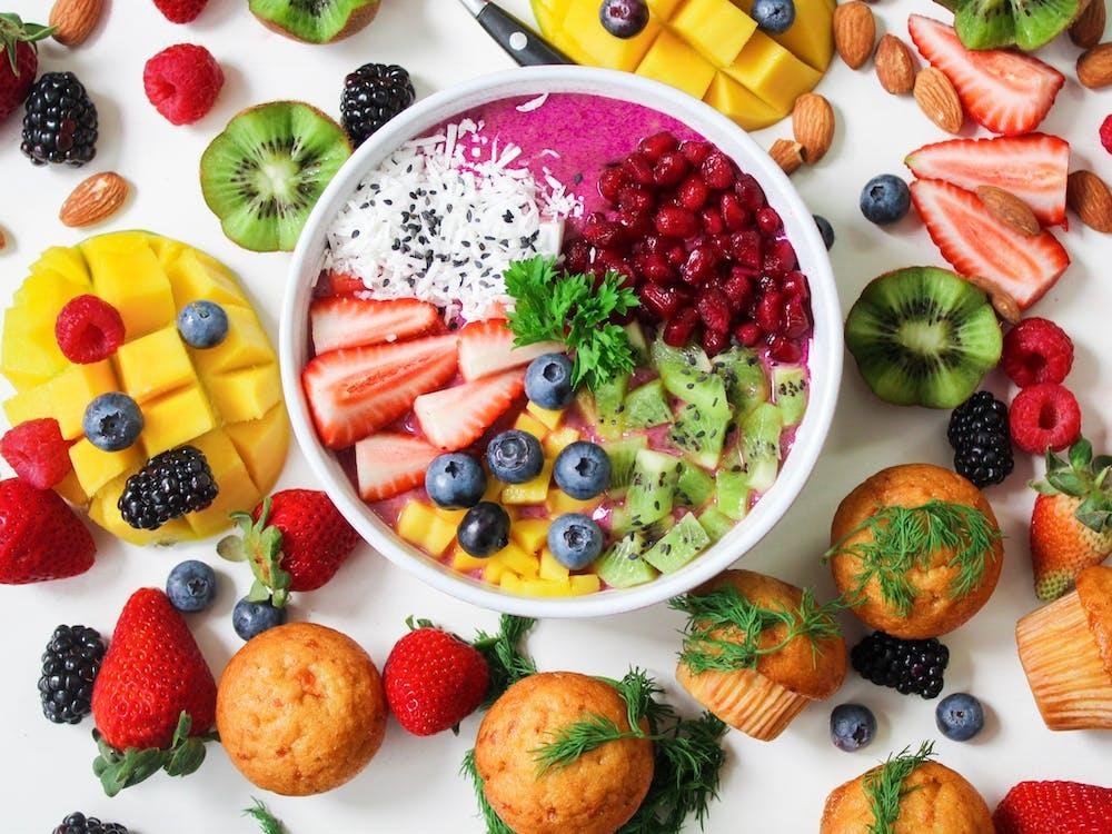 Fruit bowl with kiwi, strawberries, mango and blackberries surrounded by fresh fruit and muffins