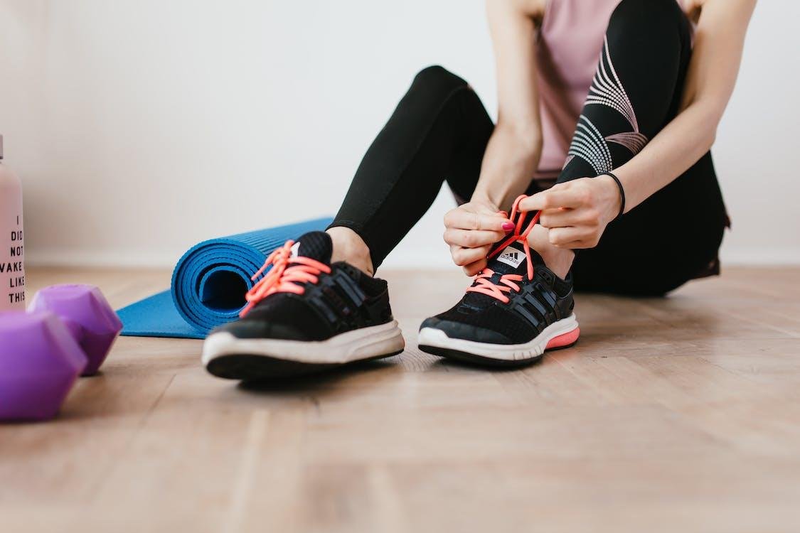 Person tying the laces of their sneakers next to an exercise mat and dumbbells