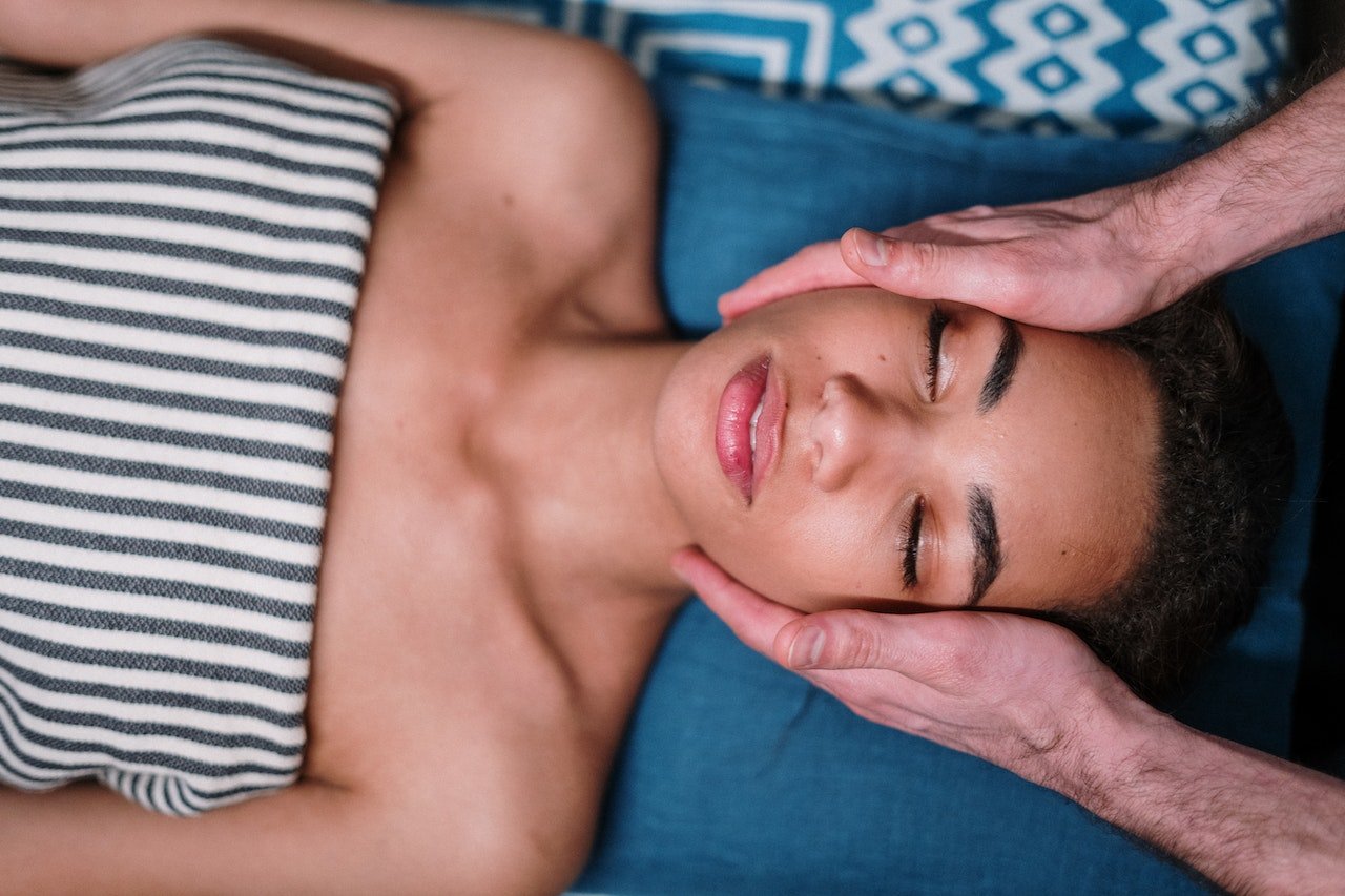 Patient lying down with her eyes closed while a professional treats her face by hand