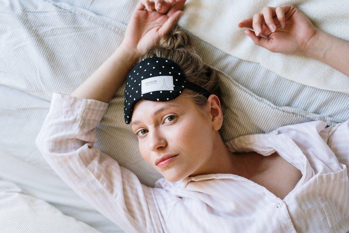 Mujer recostada en la cama con un antifaz para dormir sobre la frente