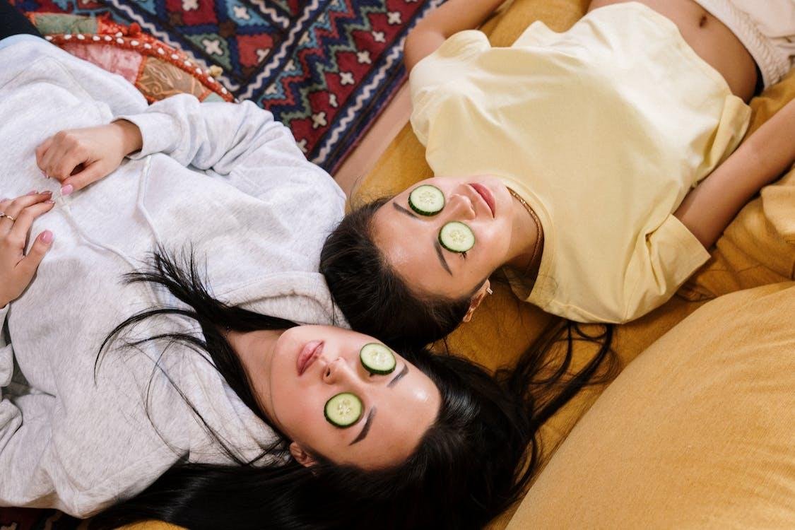 Dos mujeres recostadas con rodajas de pepino sobre los ojos