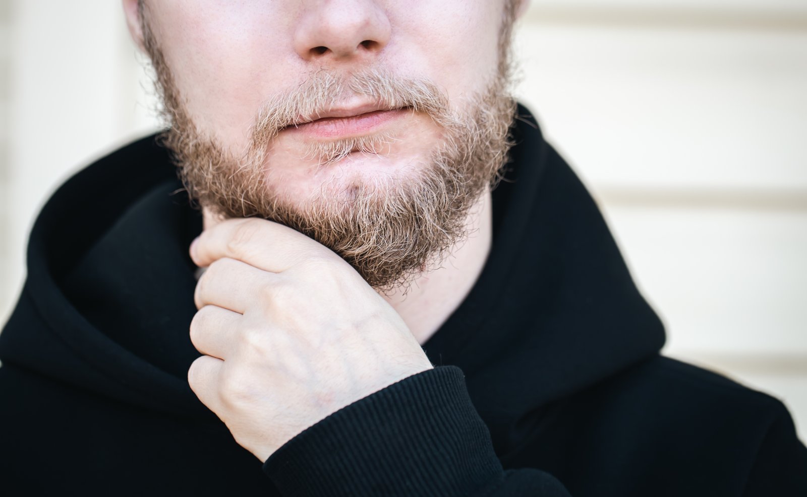 Closeup young man touches his beard with his hand · ¿Cuáles son las causas de la dermatitis seborreica?