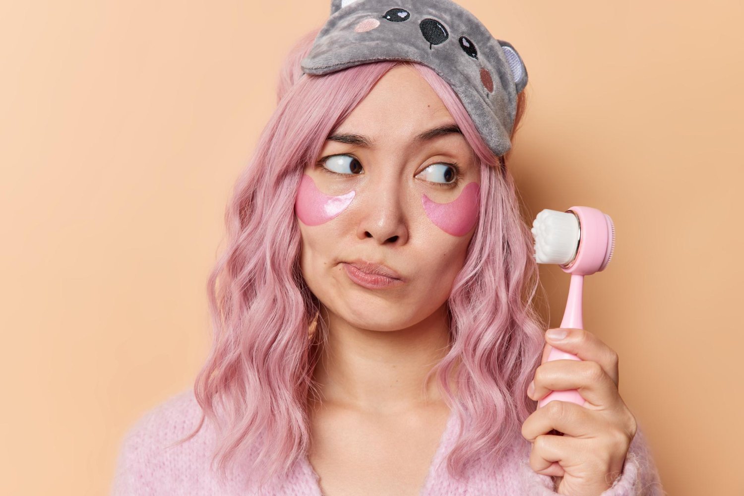 Mujer con parches bajo los ojos observa un masajeador facial eléctrico mientras decide cómo usarlo