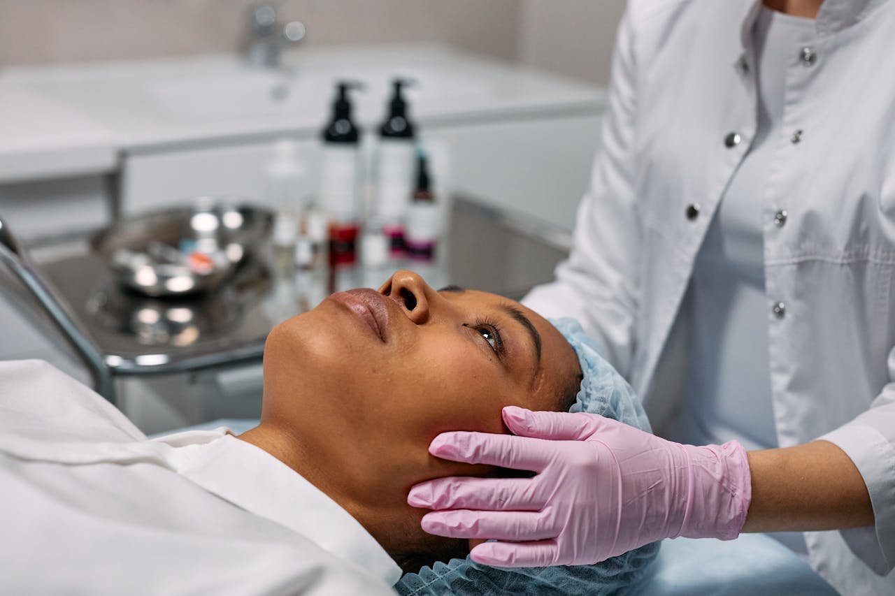 Patient lying on a treatment bed with a cap while a gloved practitioner preps the skin of her face for a HIFU session
