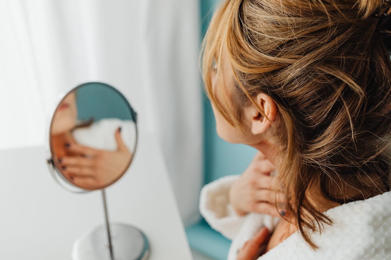 Woman seen from behind checking the firmness of her neck and jawline in a hand mirror