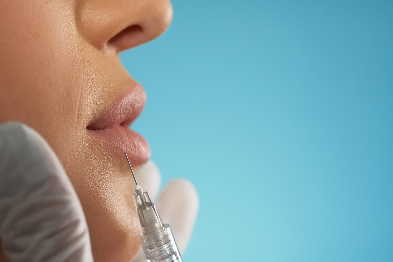 Primer plano de los labios de una paciente mientras recibe una inyección de ácido hialurónico sobre fondo azul