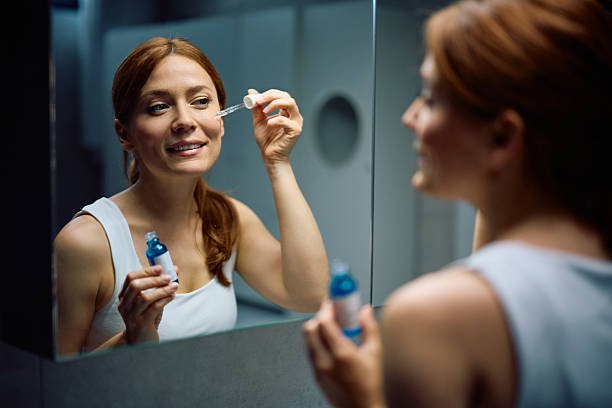 Mujer aplicándose un sérum de retinol con gotero frente al espejo del baño